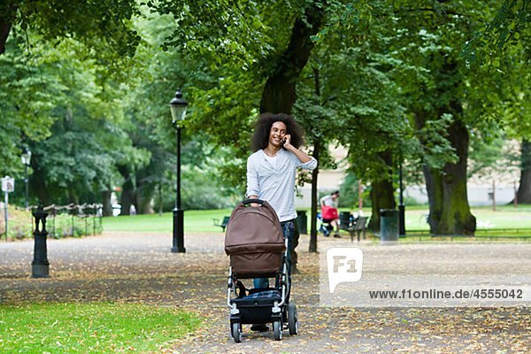 Junger Mann stossend Kinderwagen im Park und am Handy sprechen