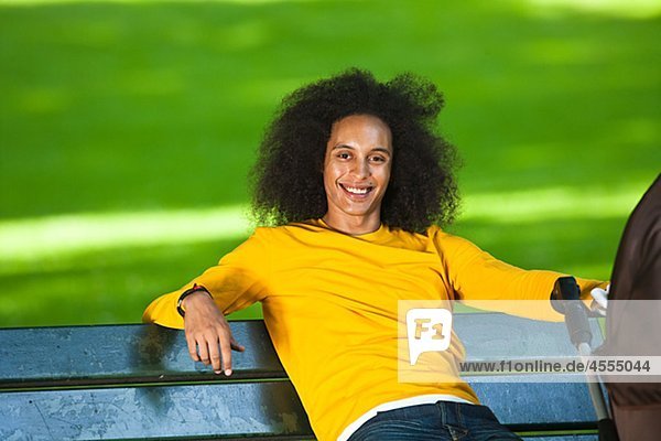 Lächelnd junger Mann mit Afro Haar entspannenden auf Bank