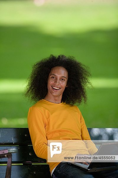 Jungen Mann lächelnd mit Afro Haar sitzen auf Bank mit laptop