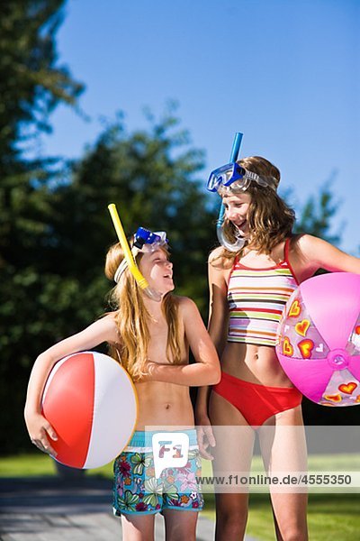Sisters in scuba mask holding beach balls and looking at each other