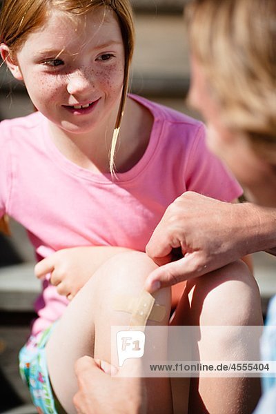 Father sticking adhesive bandage on his daughters knee