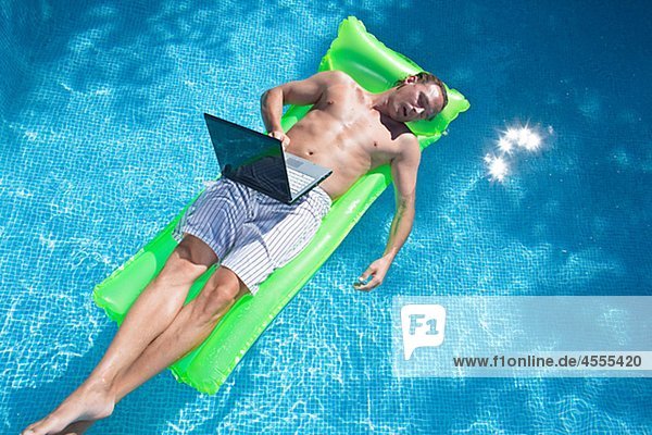 Man floating on inflatable raft with laptop and sleeping