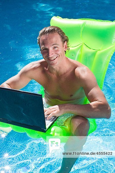 Man sitting on inflatable raft and working on laptop