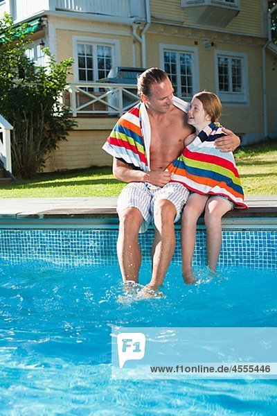 Father and daughter sitting at the edge of swimming pool