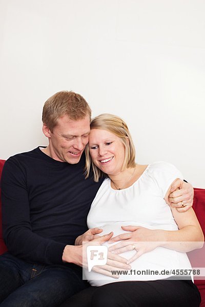 Mann mit schwangere Frau sitzt auf Sofa an Hand auf den Bauch