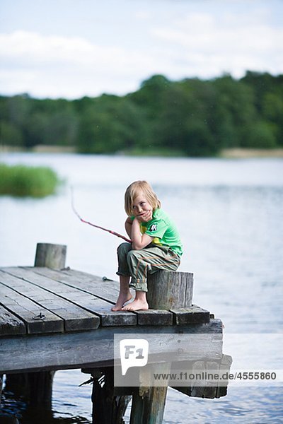 Bored boy sitting on jetty with fishing rod