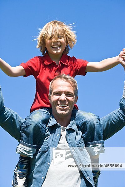Piggyback Portrait von Vater und Sohn gegen Wolkenloser Himmel in hellem Sonnenlicht