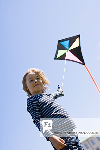 Porträt von Boy flying Kite in hellem Sonnenlicht gegen Wolkenloser Himmel