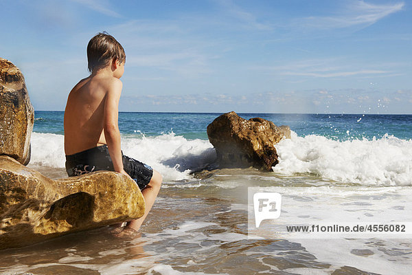 Junge sitzt auf einem Felsen und schaut aufs Meer.