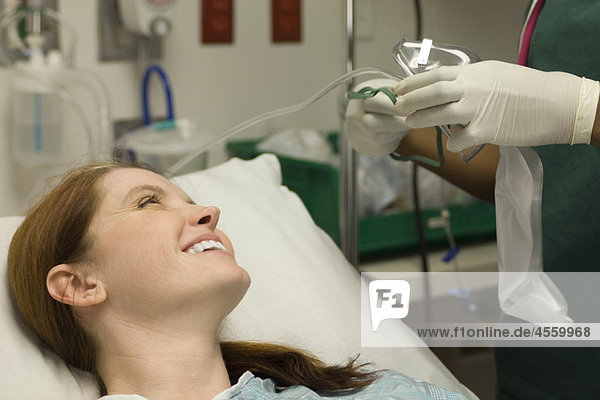 Patientin lächelt als Krankenschwester bereitet Sauerstoffmaske vor