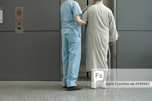 Krankenschwester hilft Patientin beim Warten auf den Aufzug im Krankenhausflur