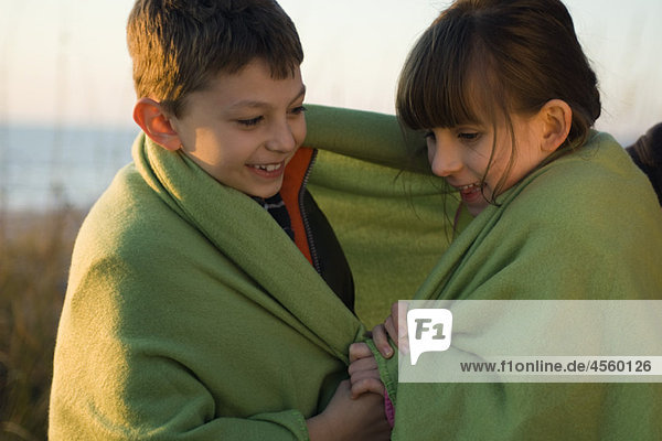 Children wrapped together in blanket outdoors  portrait