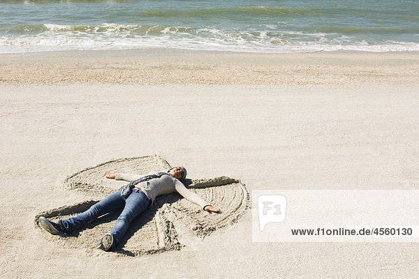 Preteen girl at beach making snow angel in sand
