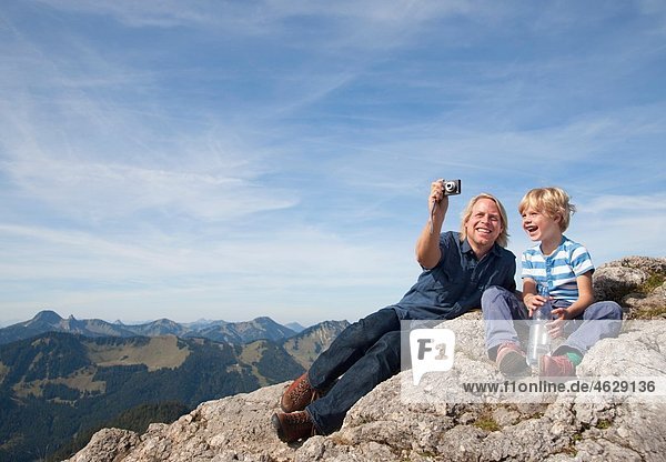 Deutschland  Bayern  Vater und Sohn (4-5 Jahre) fotografieren auf dem Berggipfel