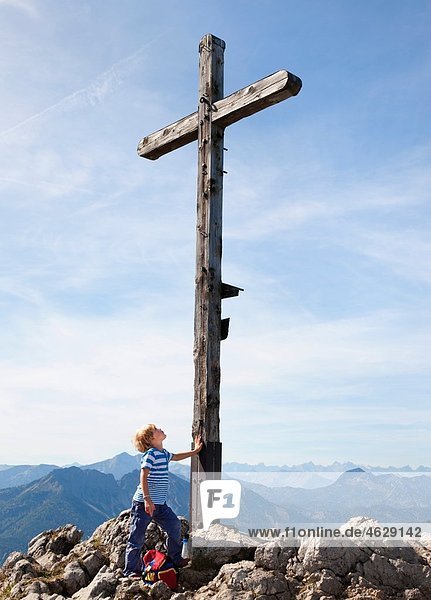 Junge (4-5 Jahre) auf dem Berggipfel mit Blick auf das Kreuz