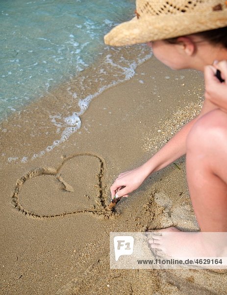 Kroatien  Zadar  Junge Frau beim Zeichnen herzförmig auf Sand am Strand