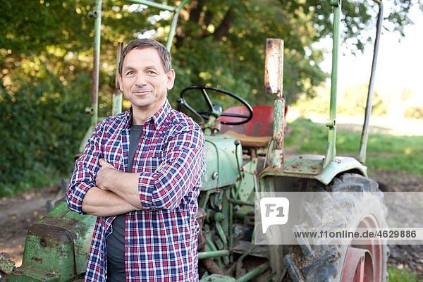 Mature man standing by tractor  smiling