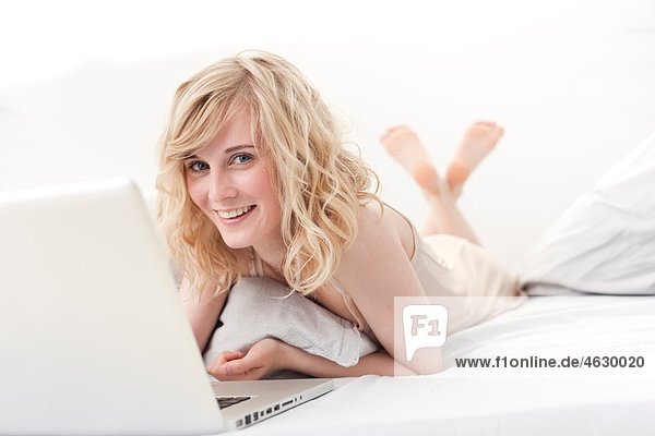 Young woman lying on bed and using laptop  smiling  portrait
