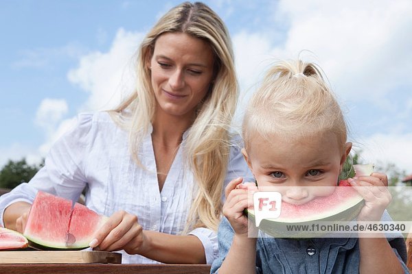 Deutschland  München  Mutter schneidet Wassermelonenscheibe für ihre Tochter (2-3 Jahre)