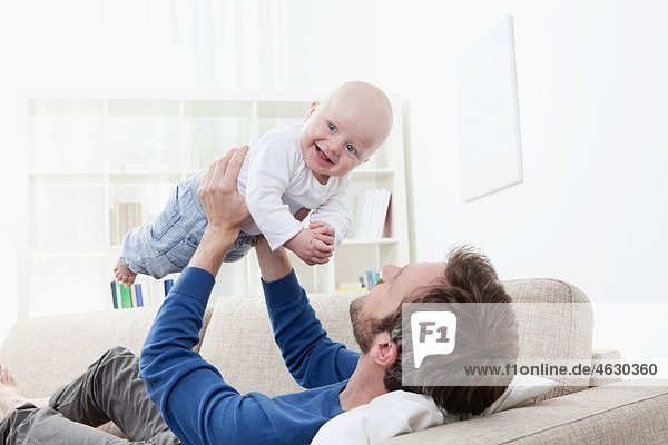 Vater spielt mit dem kleinen Jungen (6-11 Monate) auf dem Sofa.