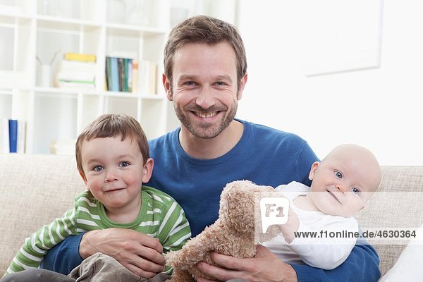 Deutschland  Bayern  München  Vater mit seinen Kindern auf dem Sofa  lächelnd