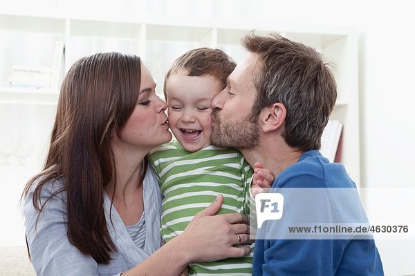 Eltern küssen Jungen (2-3 Jahre) im Wohnzimmer