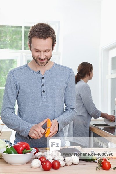 Mann schält Karotte in der Küche  Frau im Hintergrund