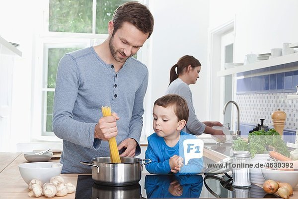 Deutschland  Bayern  München  Vater und Sohn (2-3 Jahre) kochen Spaghetti und Mutter im Hintergrund