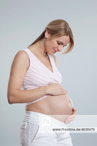 Eine schwangere erwachsene Frau  die ihren Bauch beobachtet.