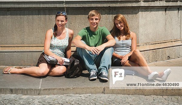 Junger Mann und junge Frauen sitzen am Brunnen der Universität