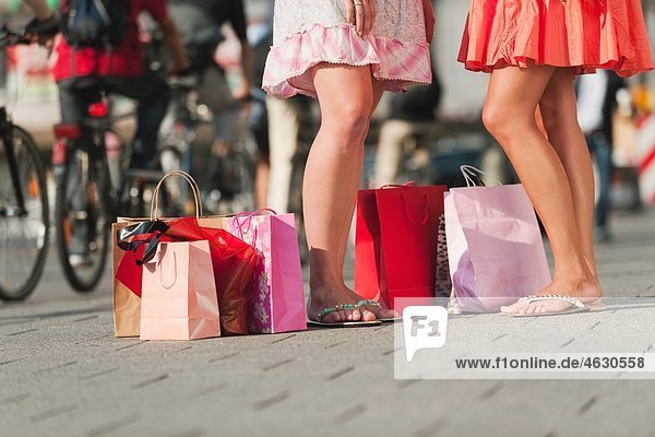 Young women waiting on footpath with shopping bags