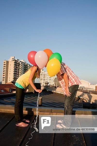 Deutschland  Bayern  München  Junges Paar mit Luftballons auf dem Dach