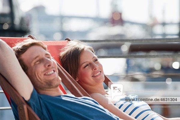 Germany  Hamburg  Couple relaxing in deck chair looking away  smiling