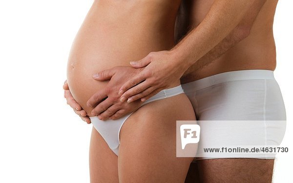 Mann  der den Bauch einer schwangeren Frau umarmt.