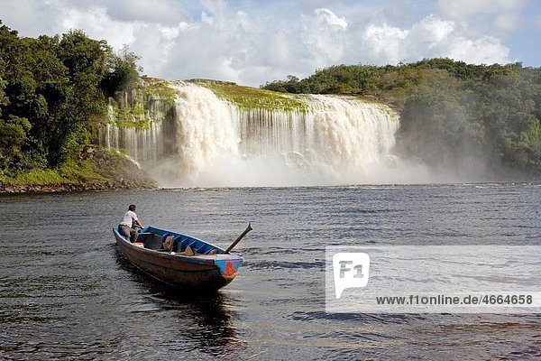 VENEZUELA GUAYANA NATIONAL PARK CANAIMA CANAIMA VILLAGE A Pemon tribe man while sailing with his boat at Canaima lake just in front of a big waterfall shoot on a bright day with blue sky and white clouds