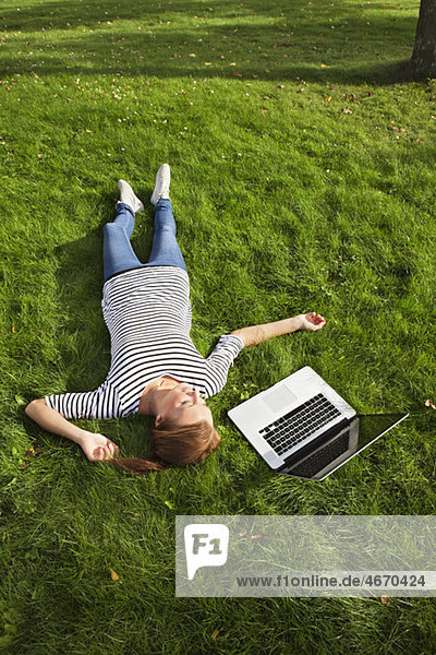 Frau im Gras neben dem Computer liegend