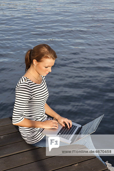 Frau am Steg sitzend mit Computer im Schoß