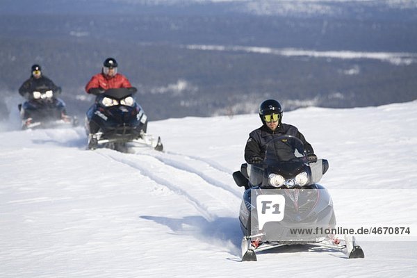 Three people driving snowmobile