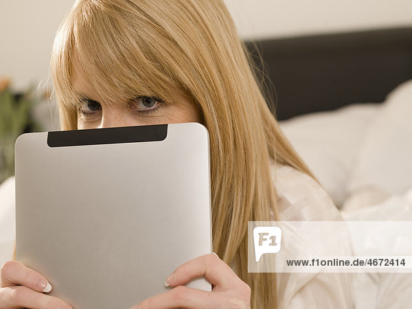 Junge Frau mit Tablet PC im Bett