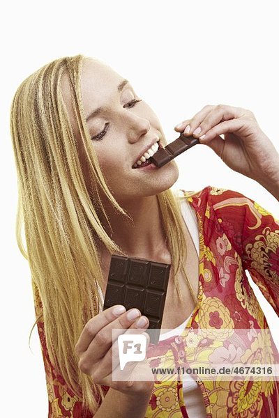 A young woman biting a piece of dark chocolate