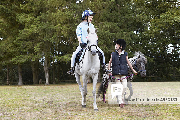 Zwei Mädchen reiten auf Ponys.