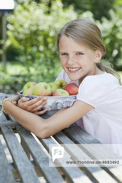 Mädchen umarmt eine mit Äpfeln gefüllte Schale