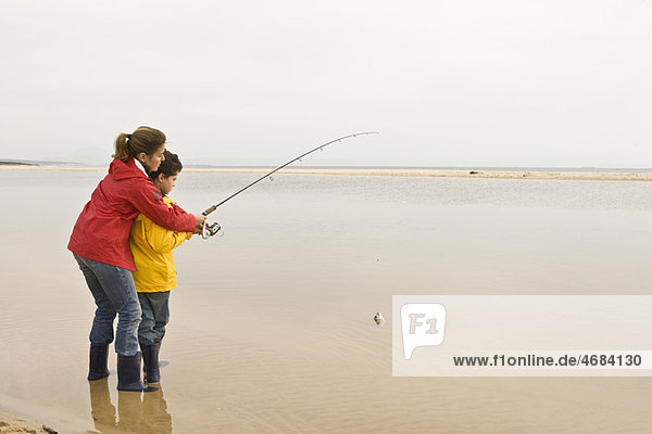 Mutter bringt dem Sohn das Fischen am Strand bei.