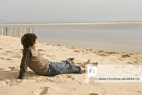 Young boy sitting on sand looking out
