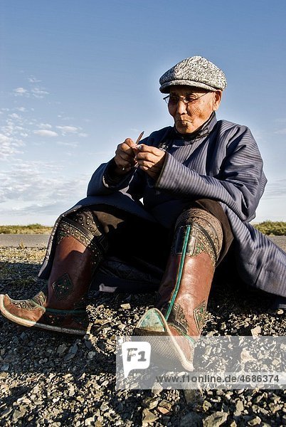 Old Mongolian man  dressed in a traditional way  eating during a rest in a long bus ride  Mongolia