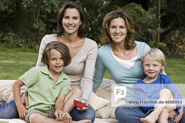 Zwei fröhliche Frauen mit zwei Kindern auf einer Decke im Freien