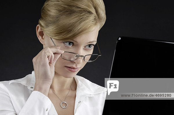 Junge Geschäftsfrau schaut überrascht über ihre Brille auf ein Computer-Display