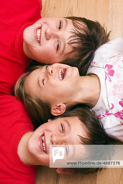 Mädchen  4 Jahre  und Jungen  6 und 11 Jahren  liegen lachend auf dem Boden
