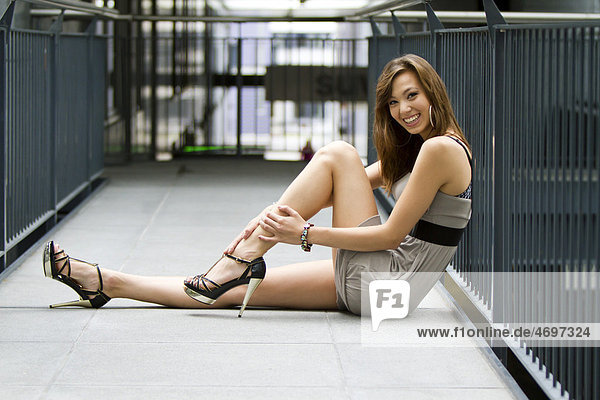 Young woman  laughing  sitting in front of a railing in a short gray dress and high heels