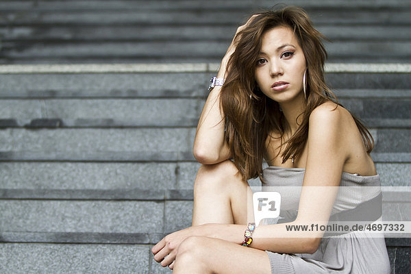 Junge Frau in kurzem grauem Kleid sitzt auf Steintreppe